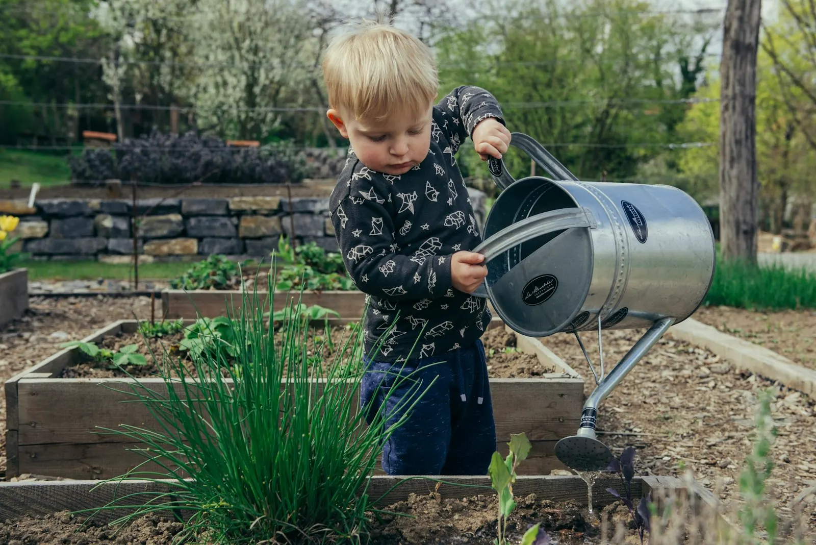 A young boy standing beside a watering can in a garden